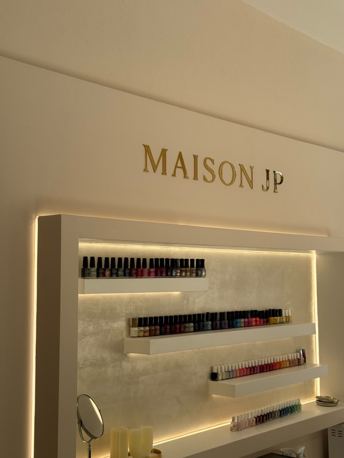 Η χρυσή επιγραφή Maison JP πάνω από τα ράφια με βερνίκια